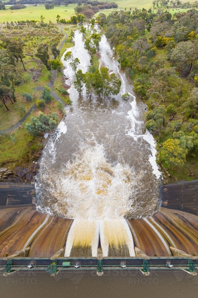 Aerial view of water spilling over a weir and down a swollen river - Australian Stock Image