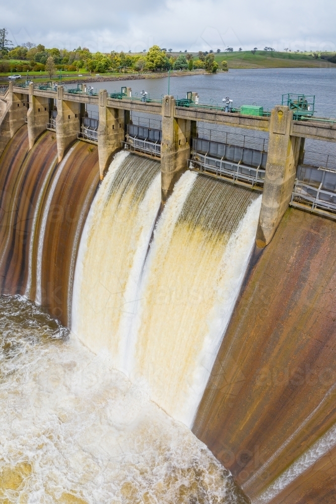 Aerial view of water spilling over a weir from a reservoir - Australian Stock Image