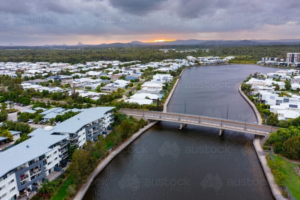 Aerial view of waterfront accommodation and a bridge over a canal under a dull sunset sky - Australian Stock Image