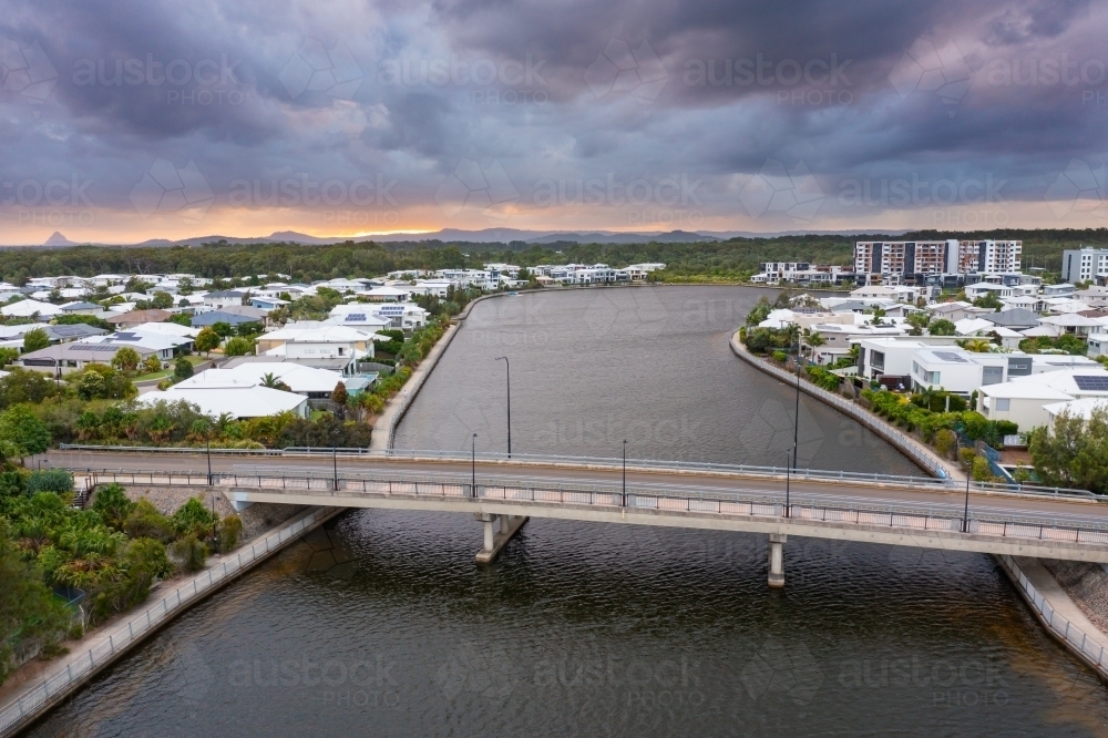 Aerial view of waterfront accommodation and a bridge over a canal under a dull sunset sky - Australian Stock Image