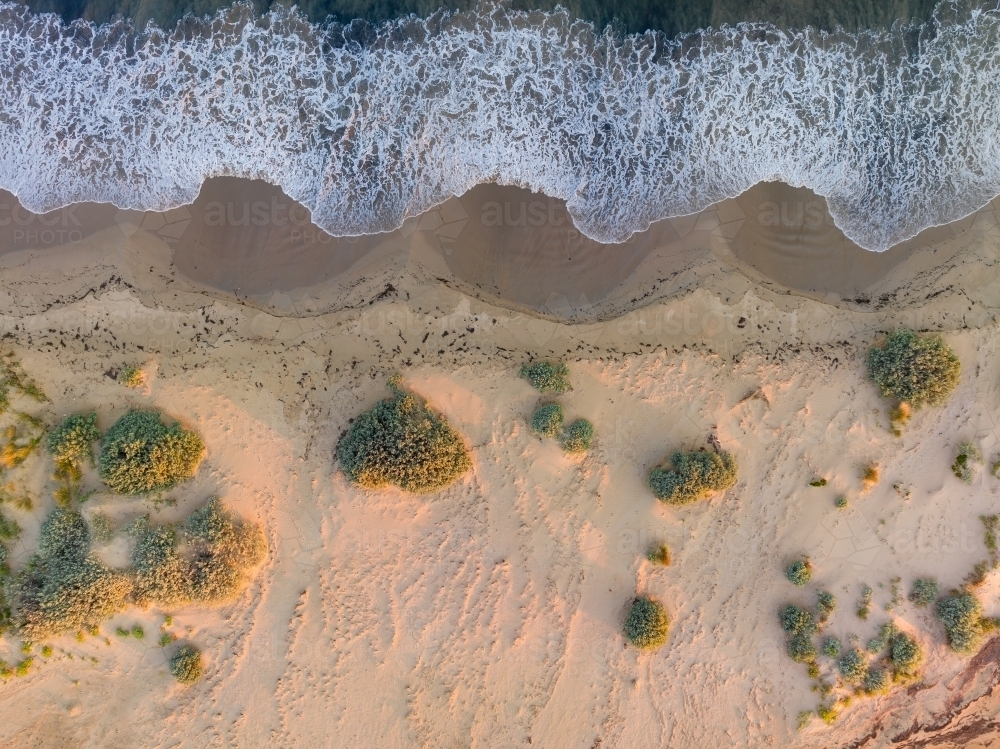 Image of Aerial view of wave patterns on a sandy beach with pockets of ...