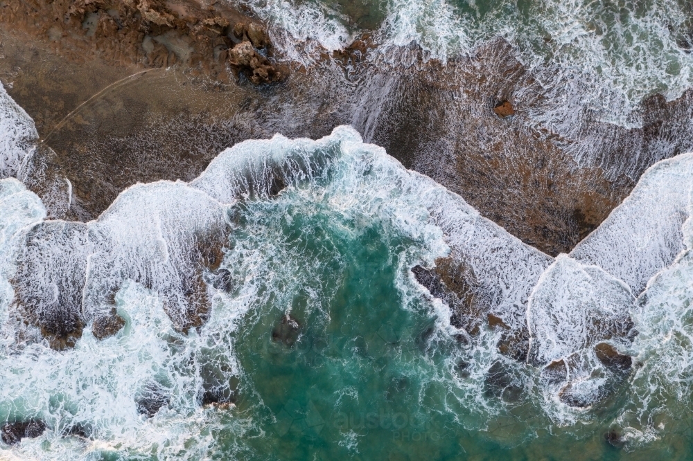 Aerial view of wave patterns over a rocky ledge on a rugged coastline - Australian Stock Image