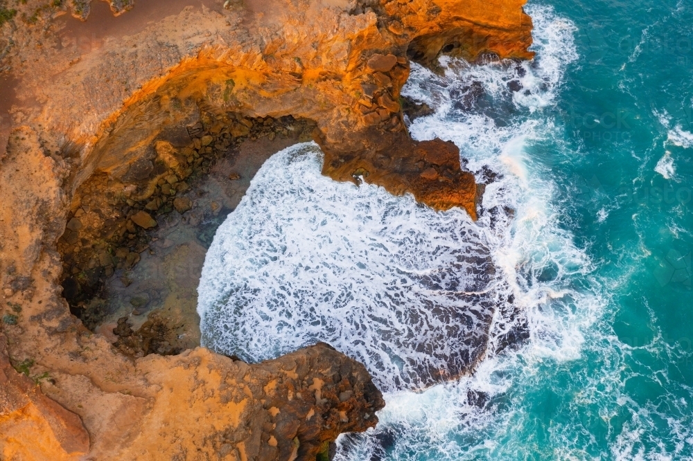 Aerial view of waves crashing against eroded cliffs along a rugged coastline at sunrise - Australian Stock Image