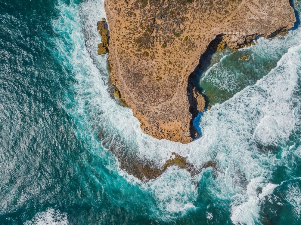 Aerial view of waves crashing against eroded cliffs along a rugged coastline - Australian Stock Image