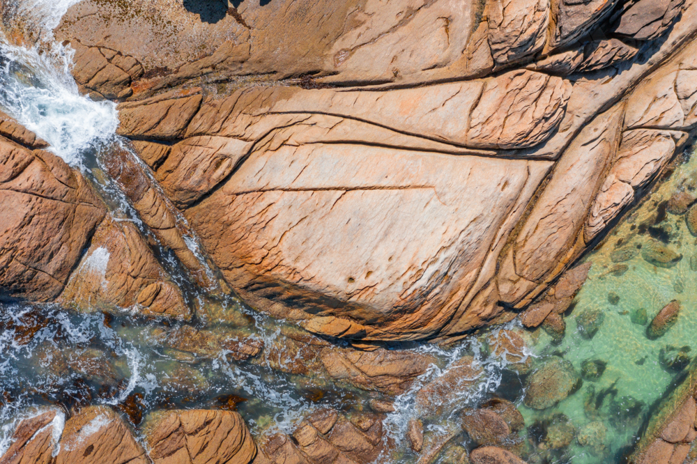 Aerial view of waves running around large granite boulders and into rockpools - Australian Stock Image