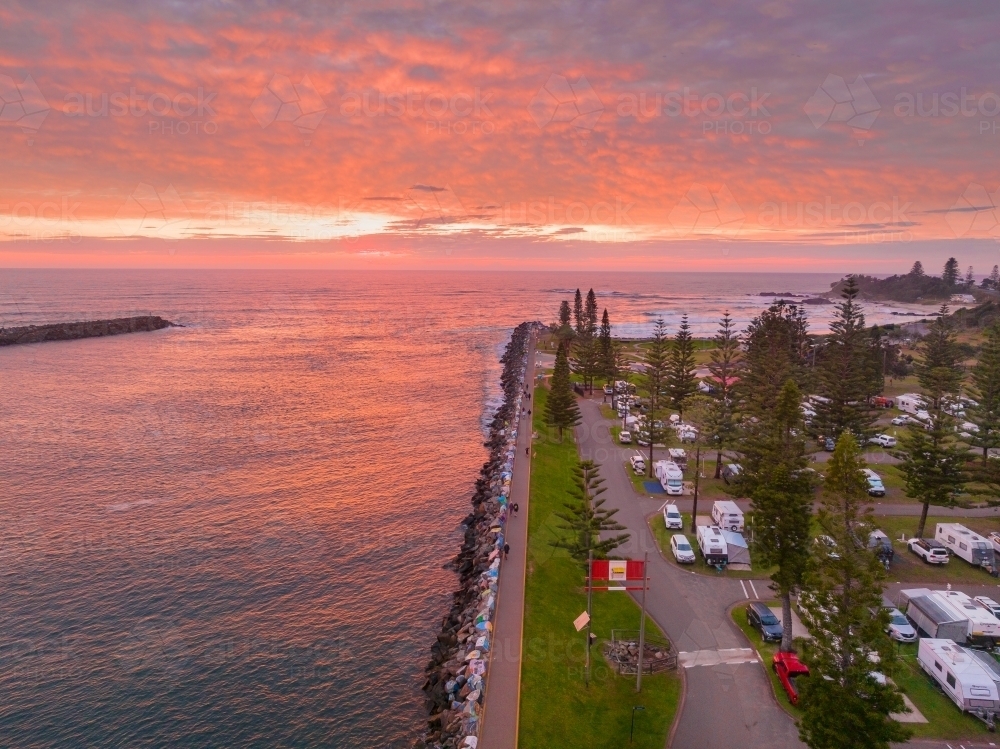 Aerial view over a riverside caravan park and breakwater under a vivid red sunrise - Australian Stock Image