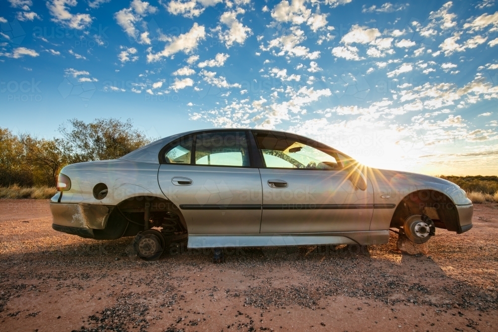 An abandoned sedan without wheels sits besides the Stuart Highway in Central Australia - Australian Stock Image