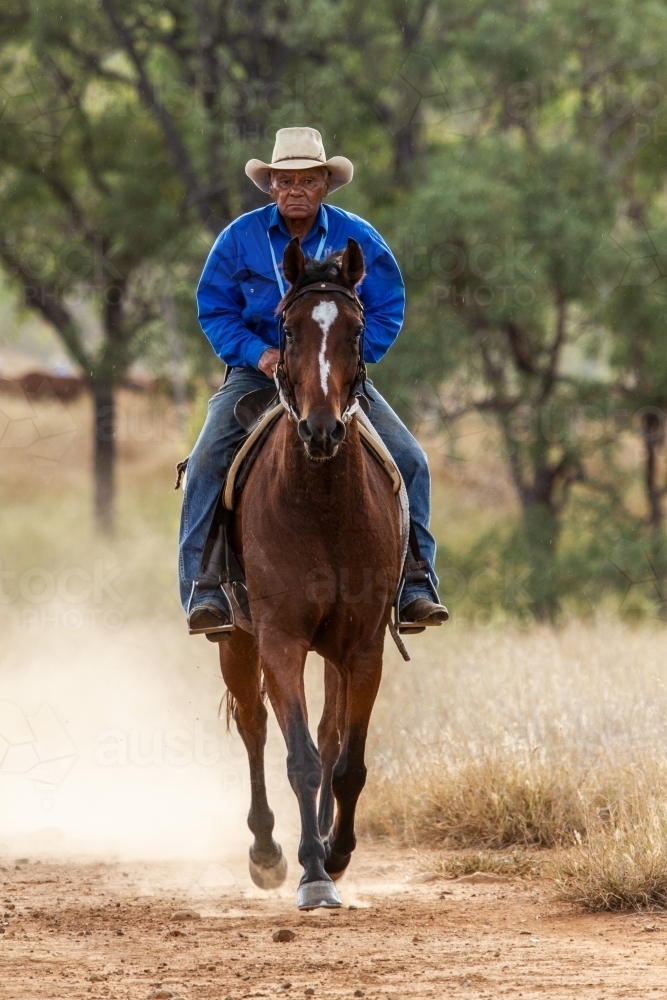 An aboriginal stockman cantering on horse. - Australian Stock Image