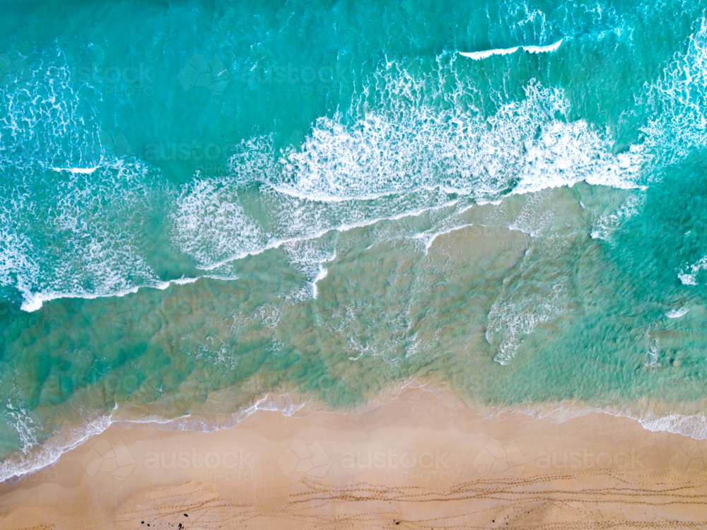 An aerial view of crumbling waves heading toward a beach - Australian Stock Image