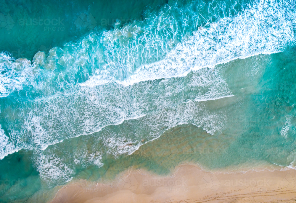 An aerial view of waves breaking onto a sandy shore. - Australian Stock Image