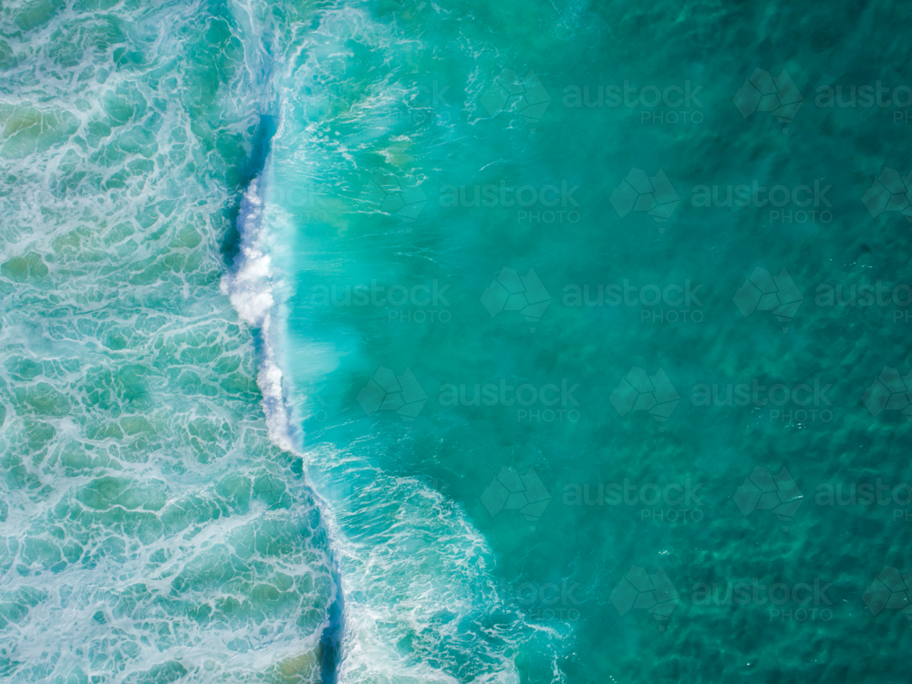 An aqua blue wave travels along crystal clear water - Australian Stock Image