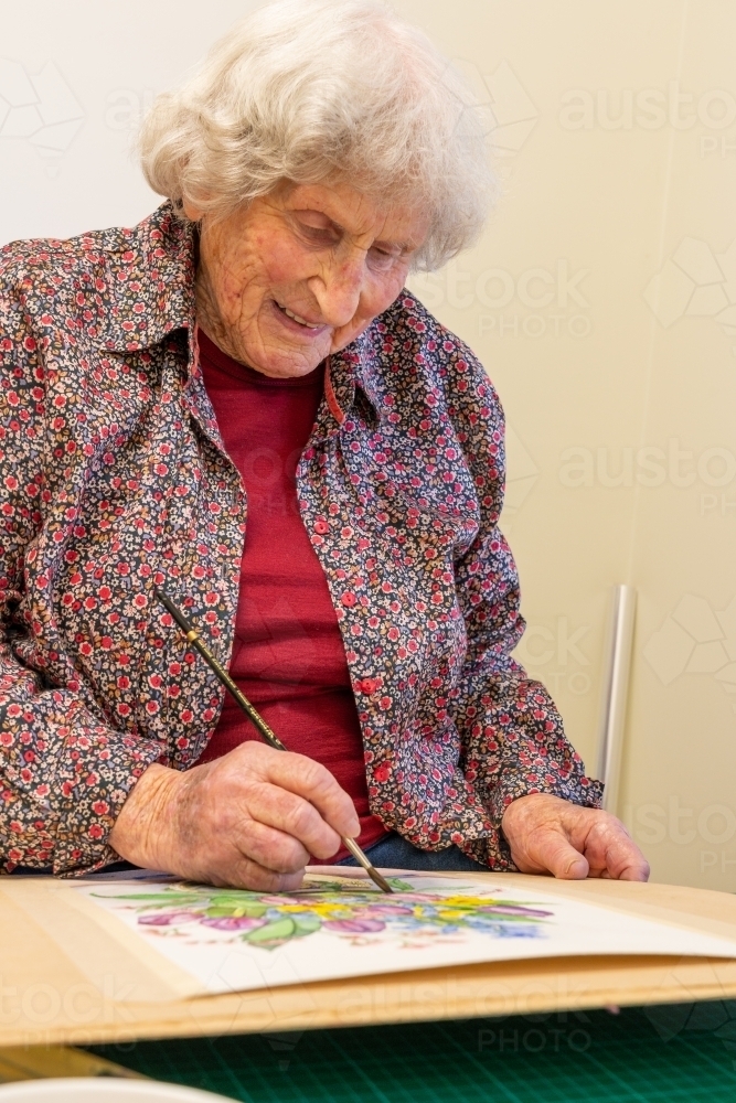 An elderly lady artist painting a water colour painting - Australian Stock Image