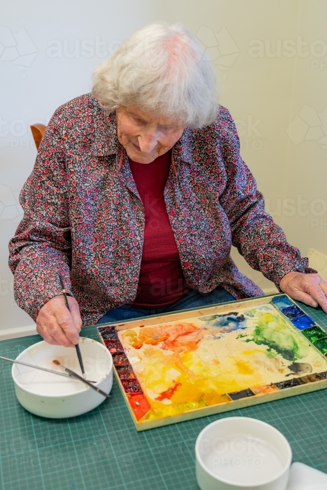 An elderly lady artist washing a paint brush in a bowl of water - Australian Stock Image