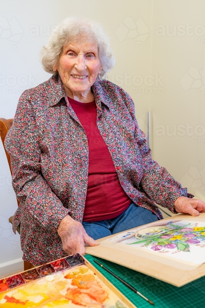 An elderly lady painter sitting with her work smiling - Australian Stock Image