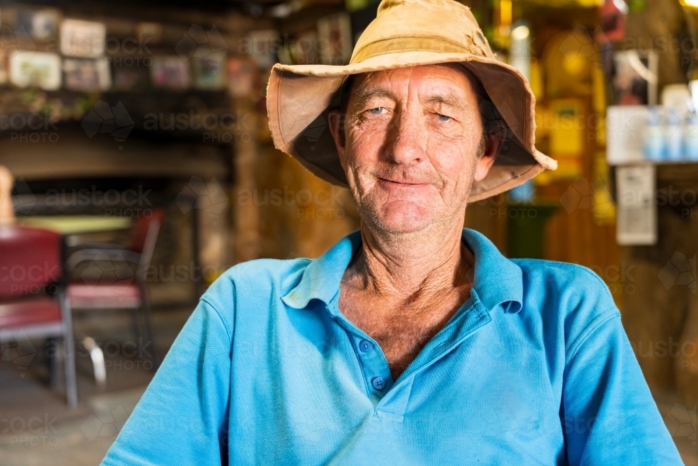 An elderly man wearing a floppy hat, sitting in an outback pub, smiling - Australian Stock Image