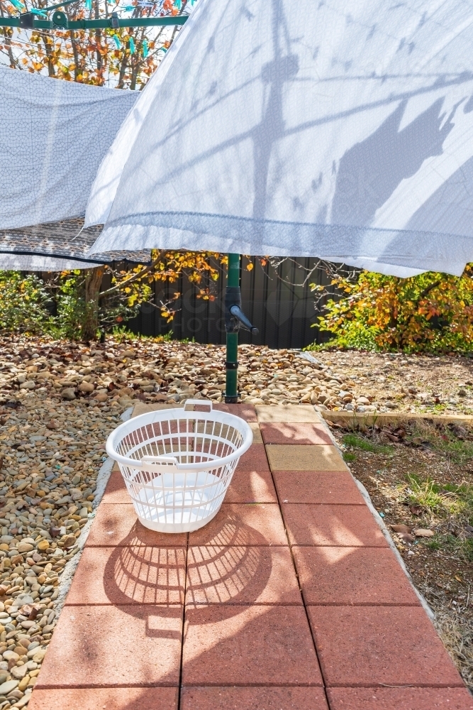 An empty clothes basket sitting on a path under washing on a clothesline - Australian Stock Image