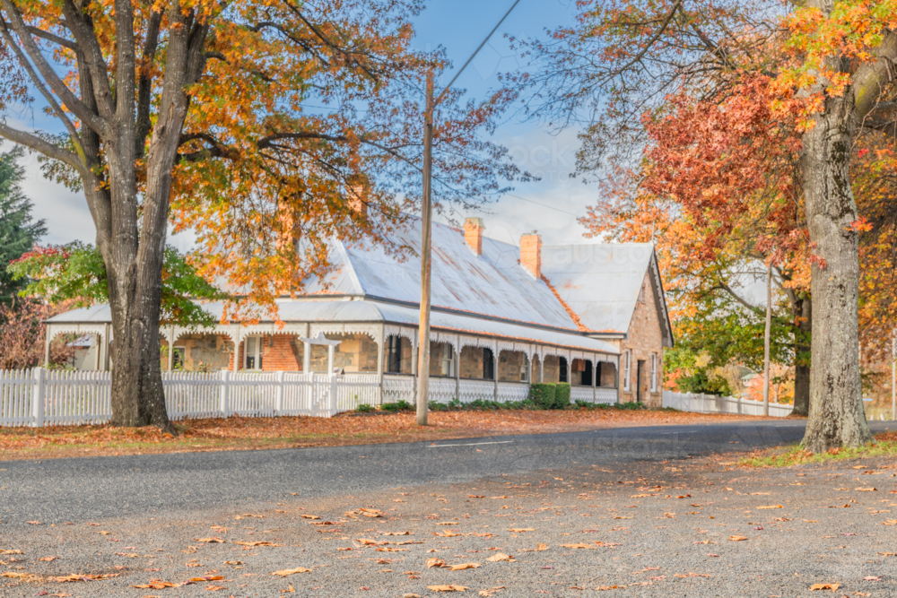 An old country home with peaked roof and white picket fence with autumn colours - Australian Stock Image