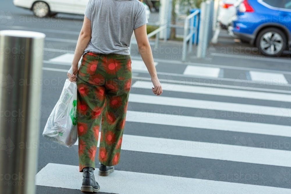 anonymous person carrying plastic shopping bag across footpath - Australian Stock Image