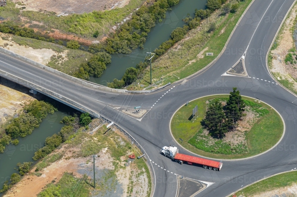 Articulated semi trailer truck going around a roundabout next to a bridge over a creek. - Australian Stock Image