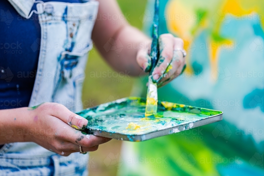 Artists hands mixing paint colours on palette - Australian Stock Image