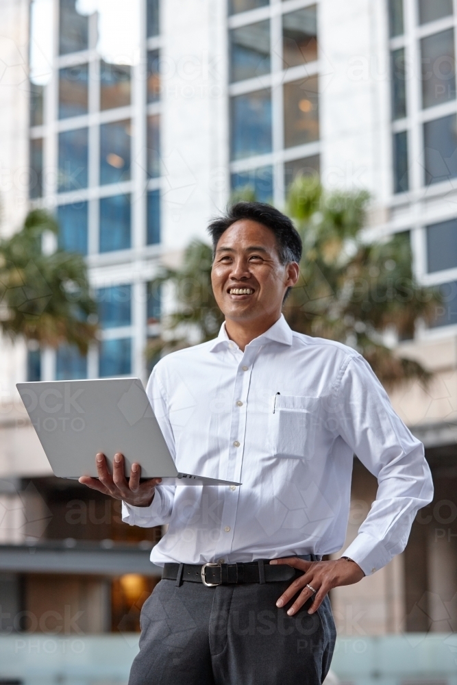 Asian businessman holding laptop in city - Australian Stock Image