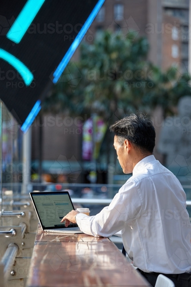 Asian businessman working on laptop in the city - Australian Stock Image