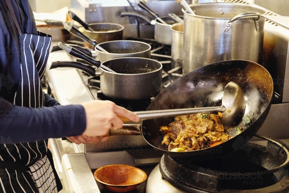 Asian chef cooking in Thai small business restaurant - Australian Stock Image