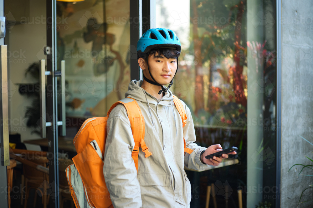 Asian delivery guy walking out of the restaurant while on his phone - Australian Stock Image