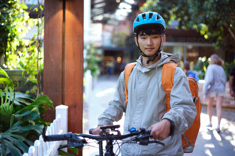 Asian delivery rider walking with his bicycle - Australian Stock Image