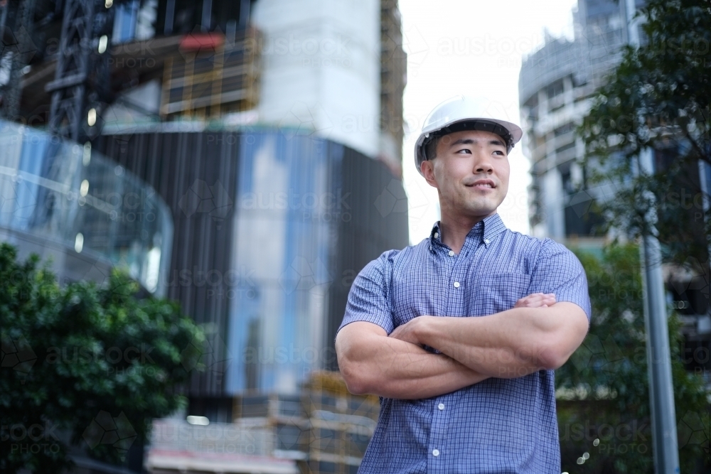 Asian man wearing hard hat with city background - Australian Stock Image