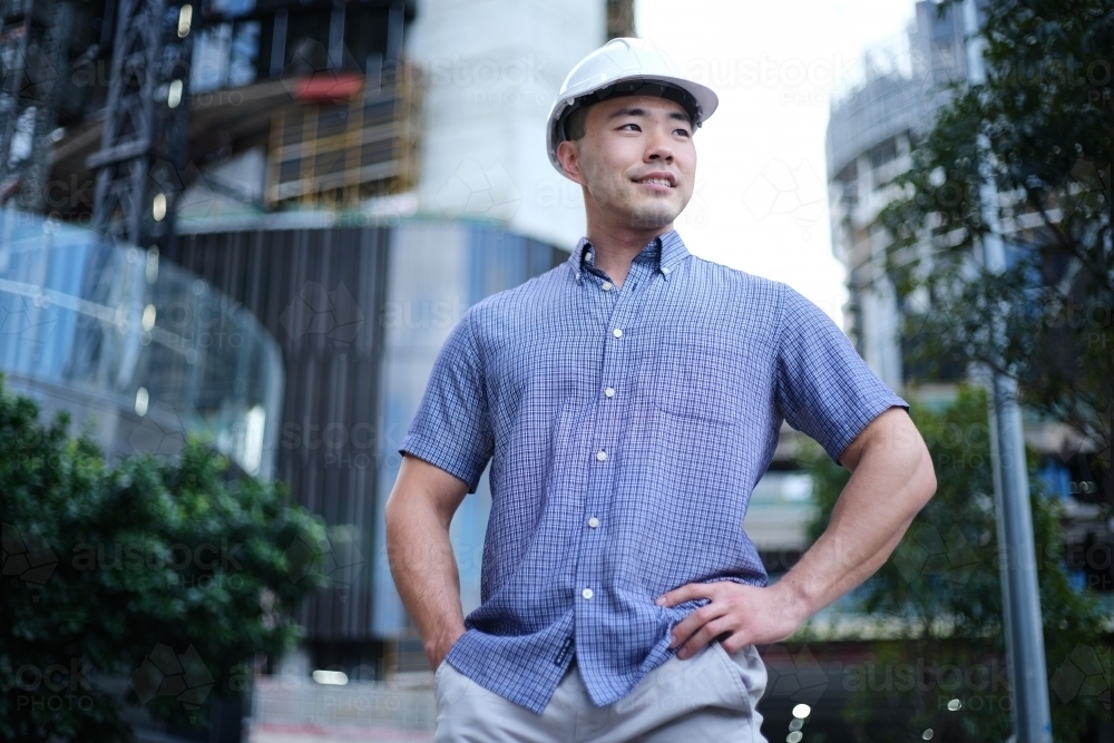 Asian man wearing hard hat with city background - Australian Stock Image