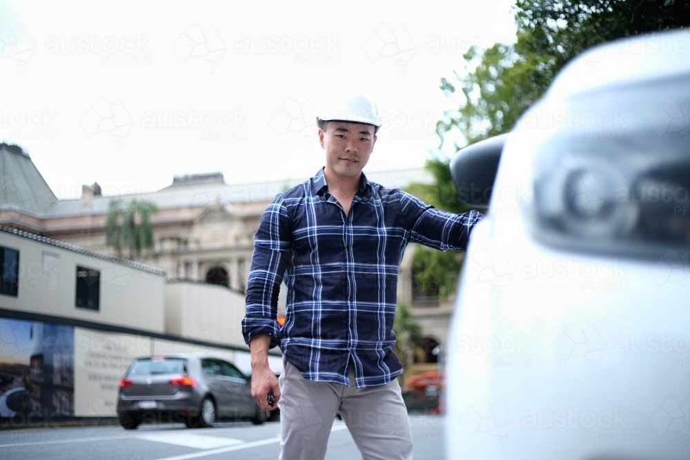 Asian man with hard hat getting into car - Australian Stock Image