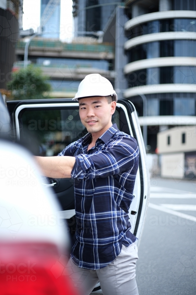 Asian man with hard hat getting into car - Australian Stock Image