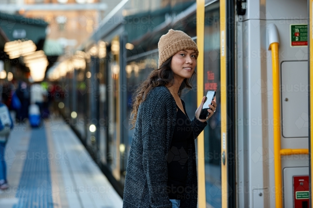 Asian woman getting on train with mobile phone - Australian Stock Image