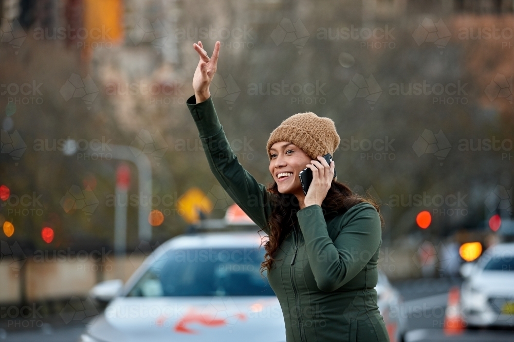 Asian woman hailing taxi with mobile phone - Australian Stock Image