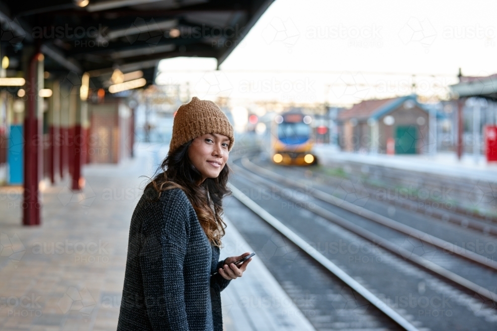 Asian woman waiting at train station with mobile phone - Australian Stock Image