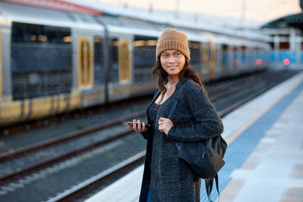 Asian woman waiting at train station with mobile phone - Australian Stock Image