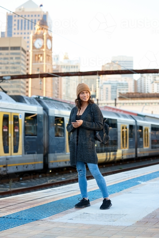 Asian woman waiting at train station with mobile phone - Australian Stock Image