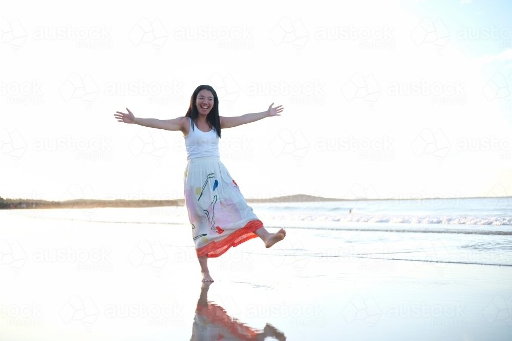 Asian woman with her arms outstretched while walking on the beach. - Australian Stock Image