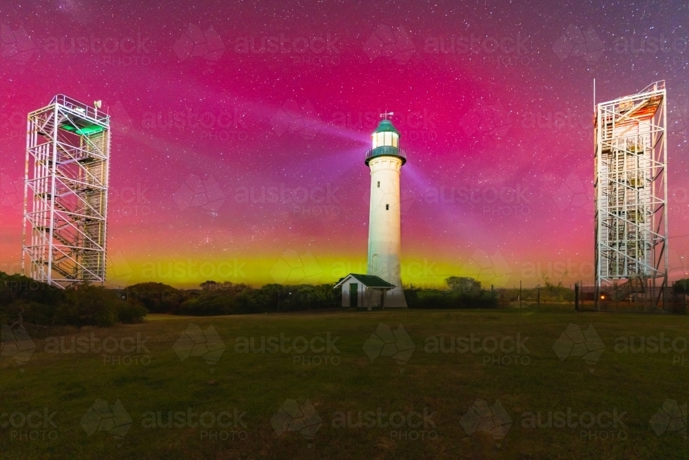 Aurora Australis filling the night sky over a tall lighthouse and nearby navigation towers - Australian Stock Image