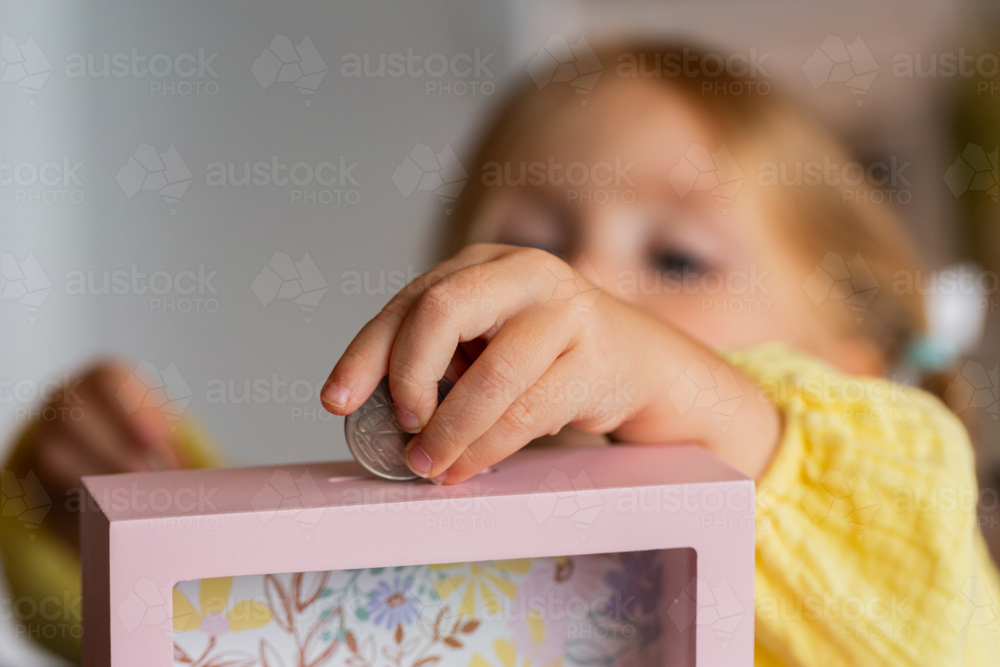 Aussie child putting Australian coin into moneybox at home - Australian Stock Image