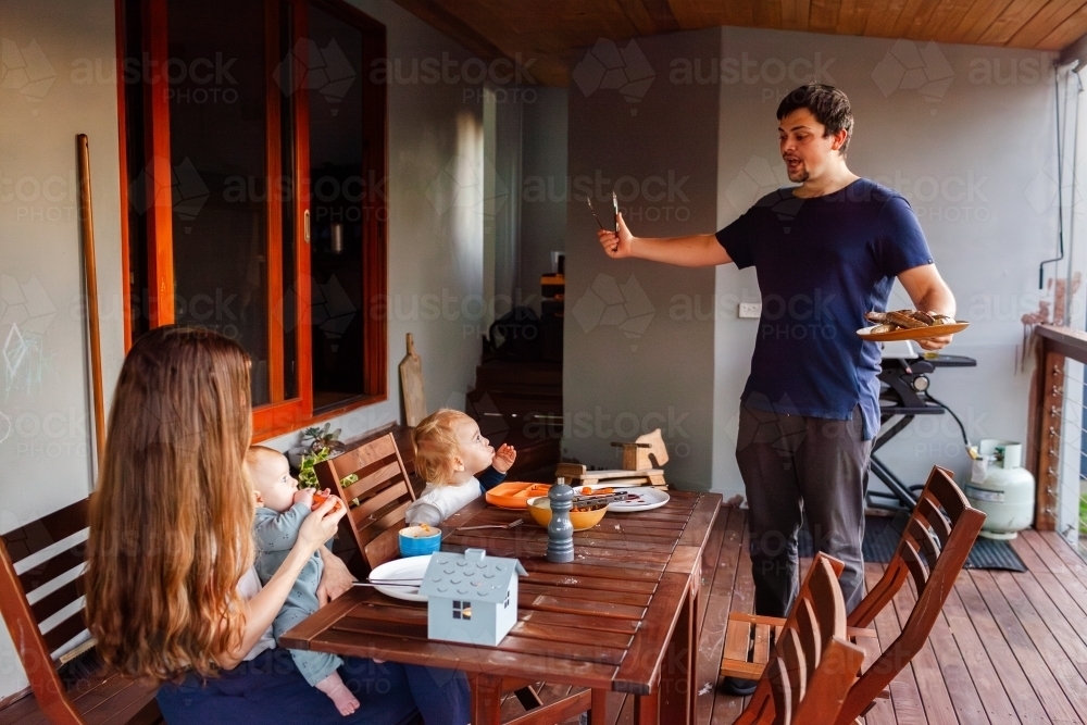 Aussie family having BBQ dinner of sausages on back deck of home - Australian Stock Image