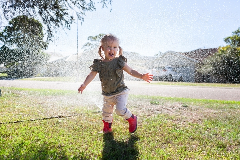 Aussie kid running through sprinkler in bright sunlight - Australian Stock Image