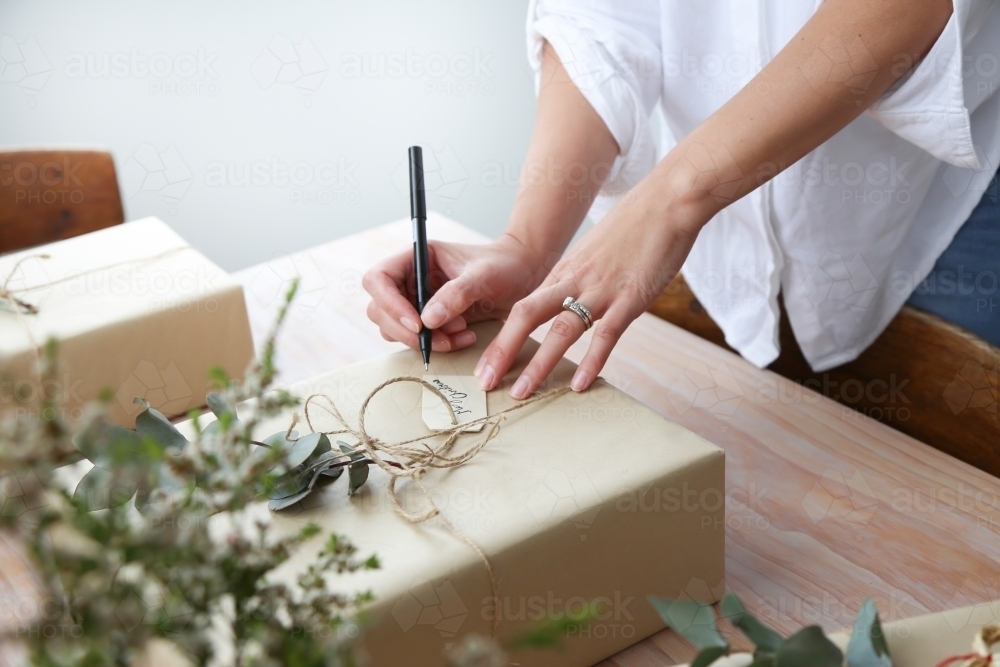 Close up of woman's hands writing gift tag for present - Australian Stock Image