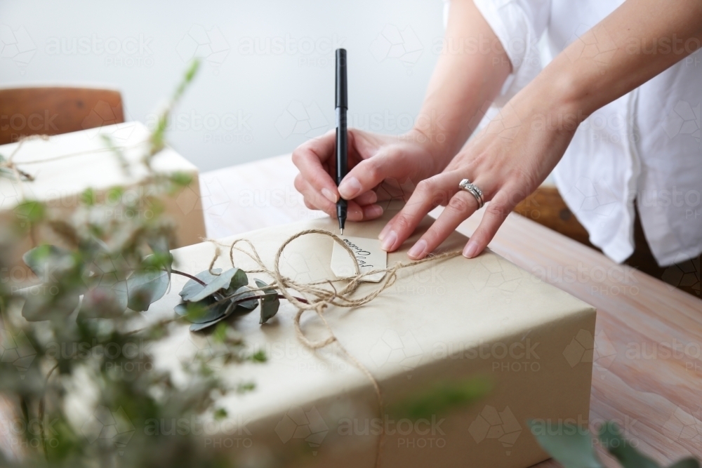 Close up of woman's hands writing gift card for present - Australian Stock Image