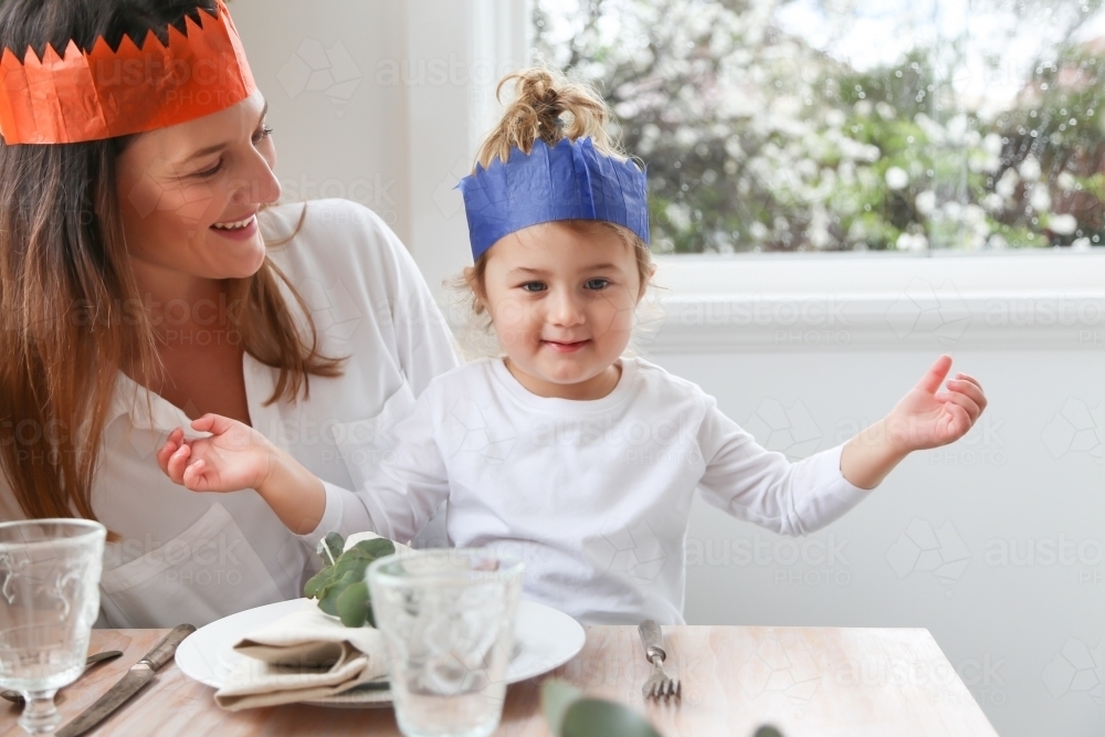 Mum with little girl at Christmas table wearing paper hats - Australian Stock Image