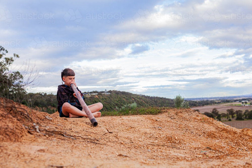 Australian cliffside landscape with aboriginal kid playing didgeridoo - Australian Stock Image