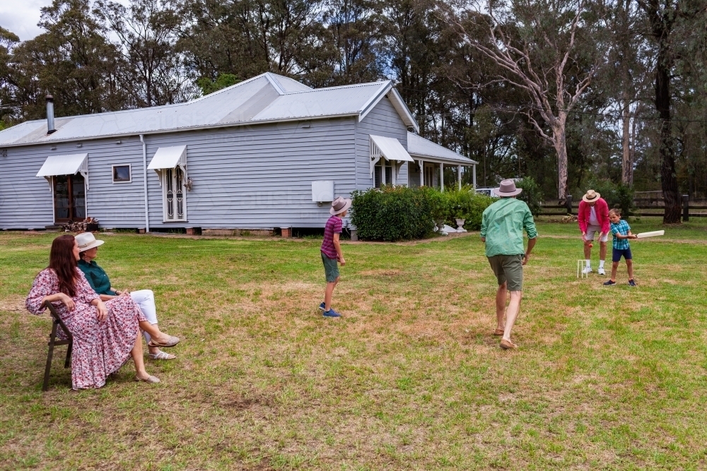 Australian family playing backyard cricket with mum and grandma watching the game - Australian Stock Image