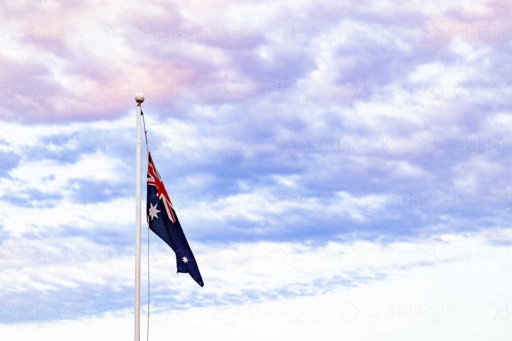 Australian flag against pastel dusk clouds colouring the sky - Australian Stock Image