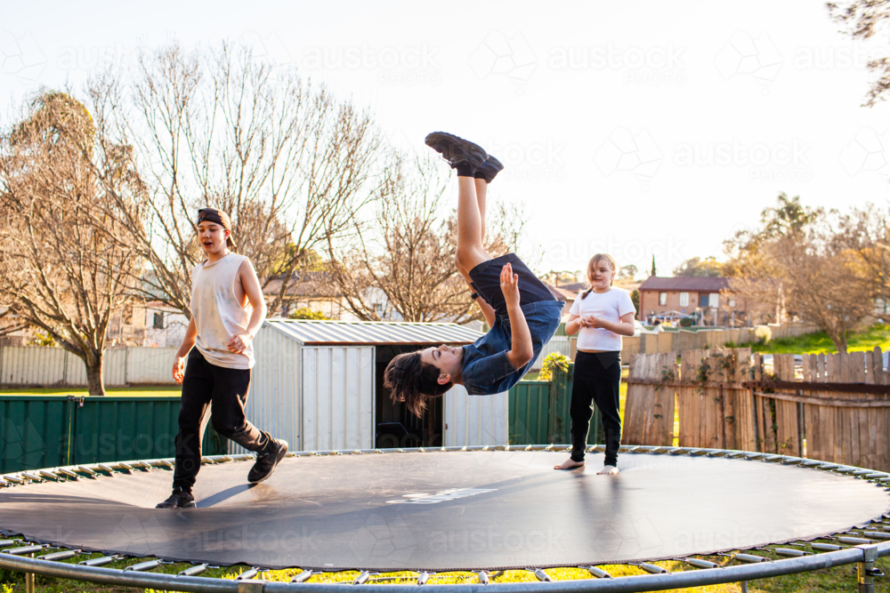 Australian kids doing backflips on a trampoline without an enclosure in backyard - Australian Stock Image